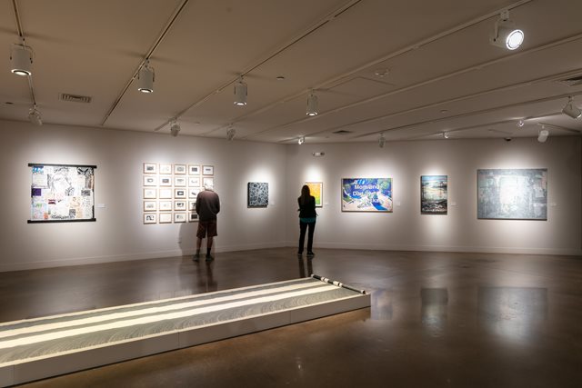 Two people look at artwork in an art gallery with white walls.