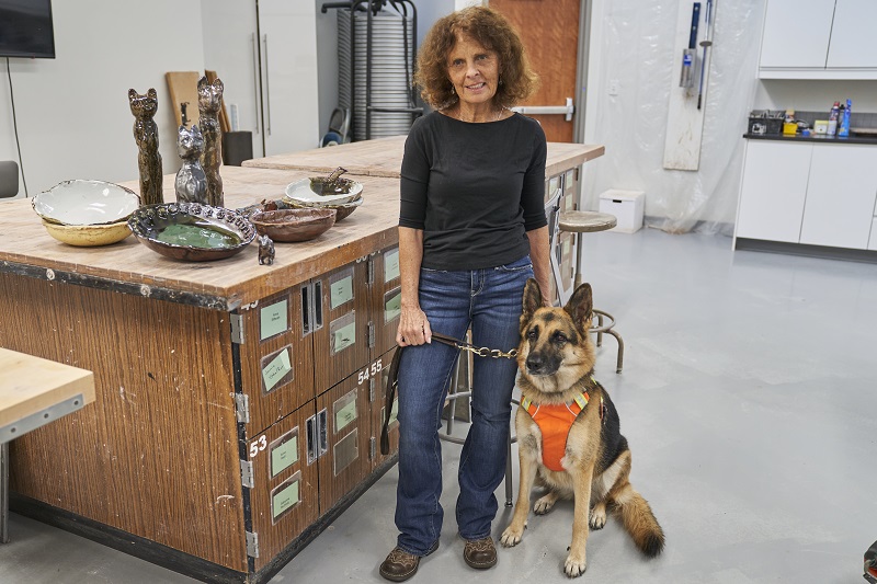 Ceramics artist and student Luanne Burke with her service dog in the Arvada Center's ceramics studio