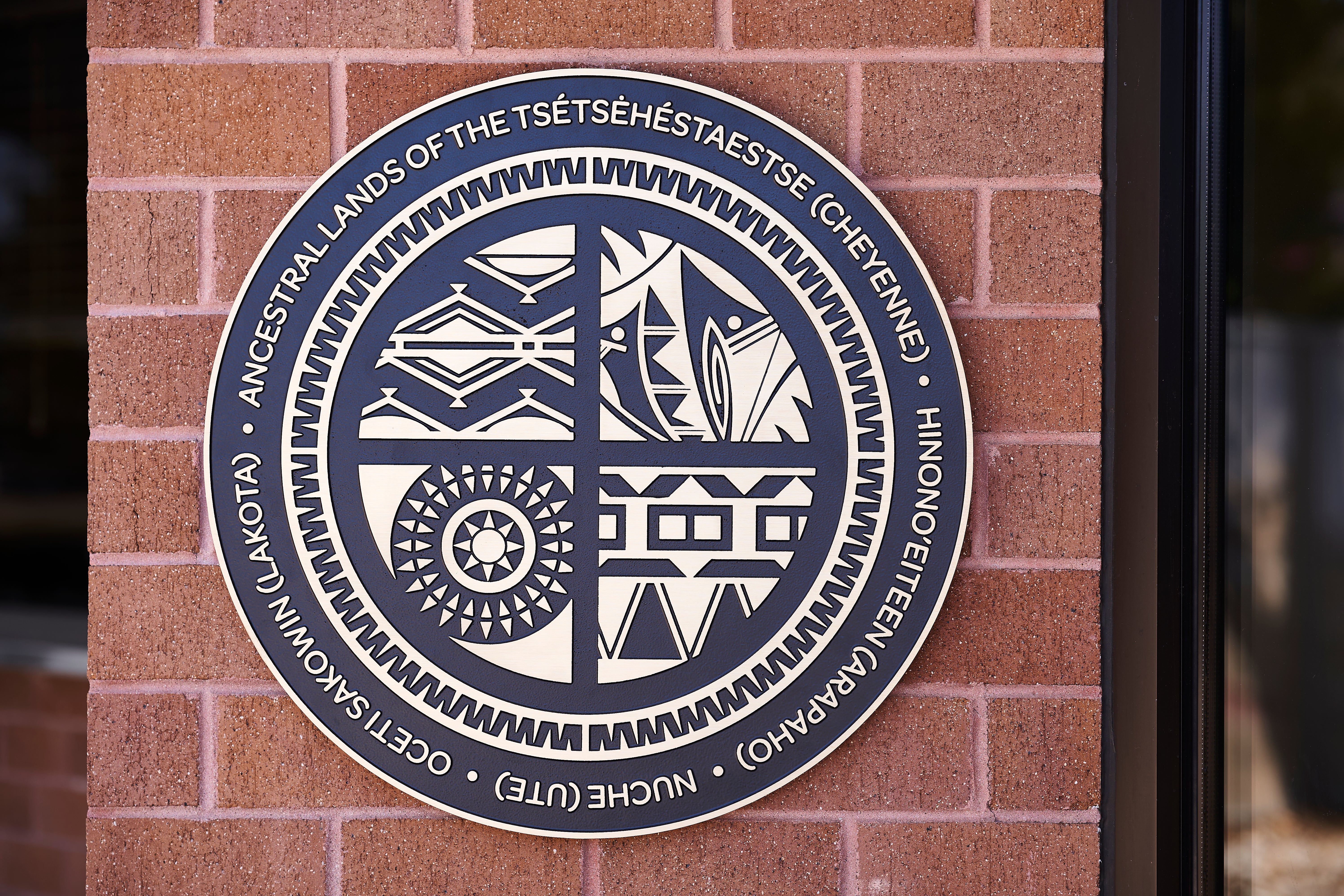 A round metal sign on the outside of the Arvada Center recognizing the land acknowledgement.